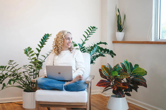 Susan Campbell sitting with her laptop in a chair surrounded by plants